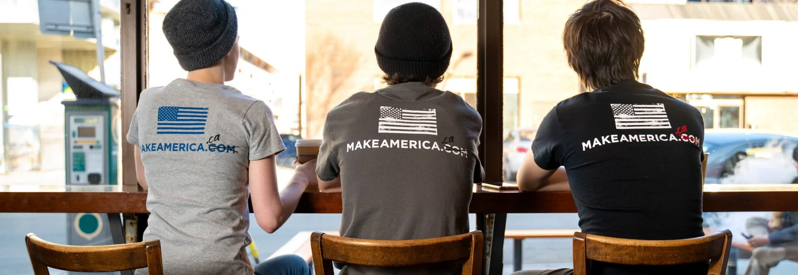 Customers at a coffee-shop window bar, seen from behind in MakeAmerica.ca branded tees