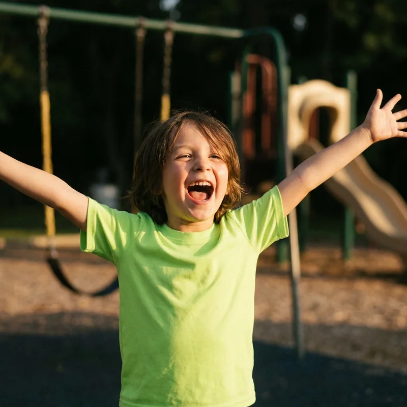 A laughing child with arms flung out on a playground